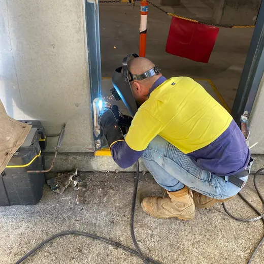 Mobile welder crouching to weld steel framing onsite